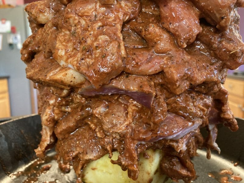 close up of marinated pork steaks layered on the grill spit